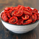 A bowl of sun-dried tomatoes, with their wrinkled texture and rich, deep red color, placed on a rustic wooden table.