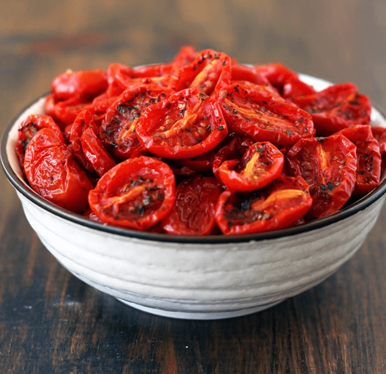 A bowl of sun-dried tomatoes, with their wrinkled texture and rich, deep red color, placed on a rustic wooden table.