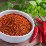 Close-up of cayenne pepper powder and whole fresh cayenne peppers on wooden surface