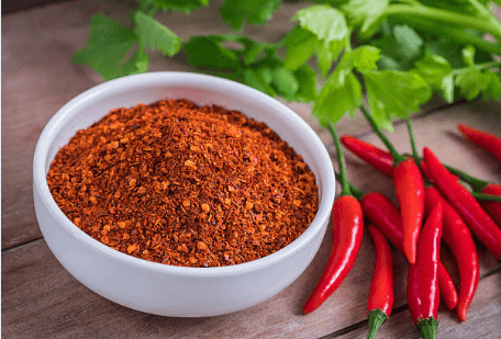 Close-up of cayenne pepper powder and whole fresh cayenne peppers on wooden surface