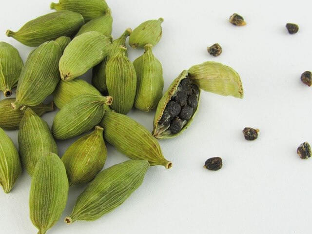 Green cardamom pods with seeds spilling out, arranged on a white surface