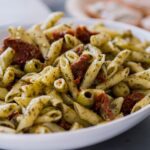 A plate of sun-dried tomato pasta garnished with fresh basil and Parmesan cheese, served on a rustic wooden table.