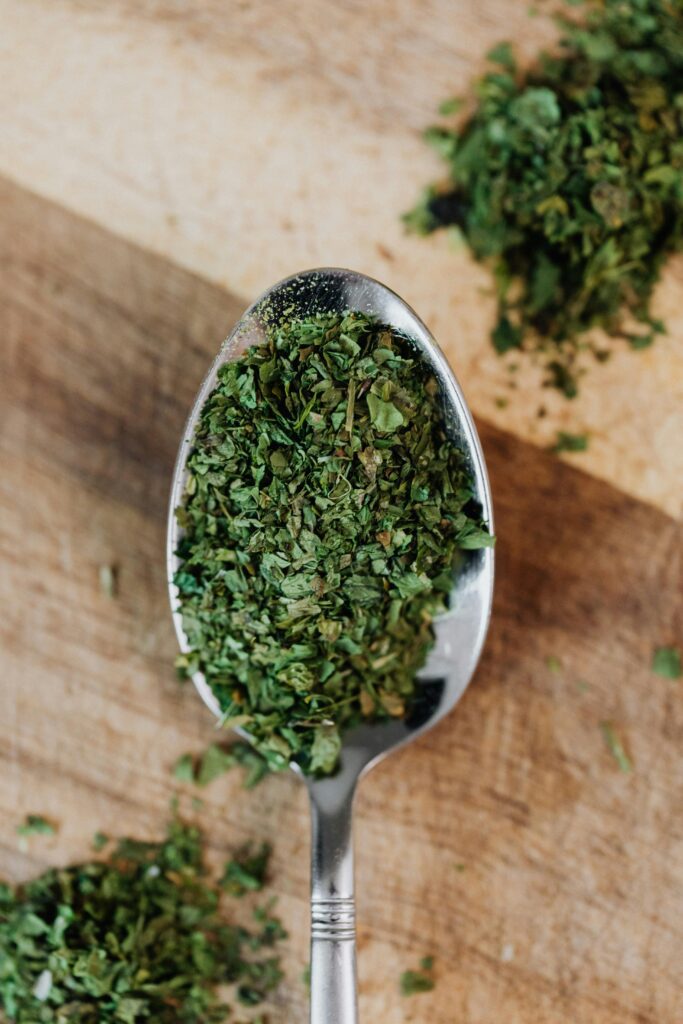 Dried oregano in a small silver spoon on the top of rustic wooden background